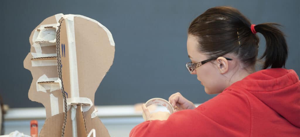 girl in red jacket working on 3-d cardboard sculpture