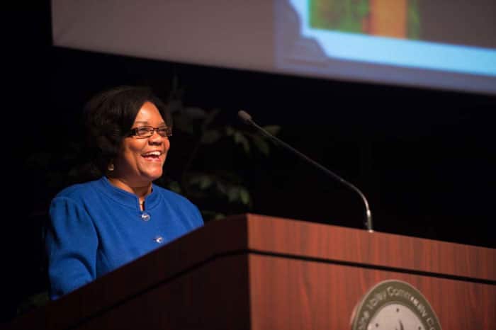 Moraine Valley Community College President Sylvia Jenkins stands behind a brown podium, smiling.