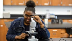A young woman looks through a microscope as part of Moraine Valley's Young Adult Career Connections Program|