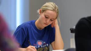 A student wearing a blue Chicago Cubs shirt takes notes during class at Moraine Valley.|A student wearing a blue Chicago Cubs shirt takes notes during class at Moraine Valley.
