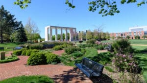 A photo of the Shakespeare Garden. A black bench sits in the foreground with the Moraine Valley Gateway in the background.