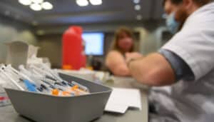 A stack of vaccine needles lay in a bowl while a nurse administers a COVID-19 vaccine to a person.