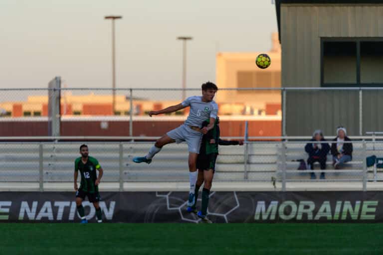 A men's soccer player jumps up to head the ball during a game