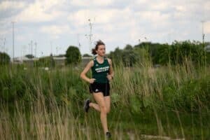 Natalia Wrobel runs outside in a grassy area wearing her Moraine Valley Cross Country uniform