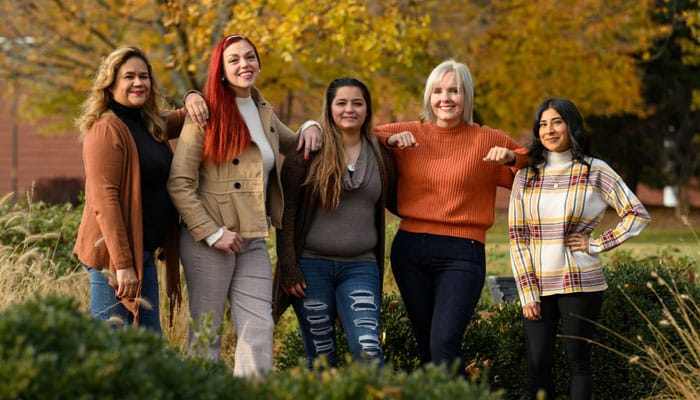 Five people standing together outdoors on campus with autumn foliage in the background
