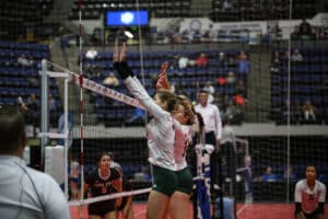 Two volleyball players jump up over the net to block a spike in a game