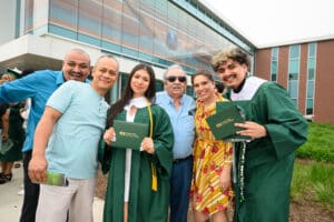 Two Moraine Valley graduates smile for a photo with their family members outside FitRec holding their diplomas