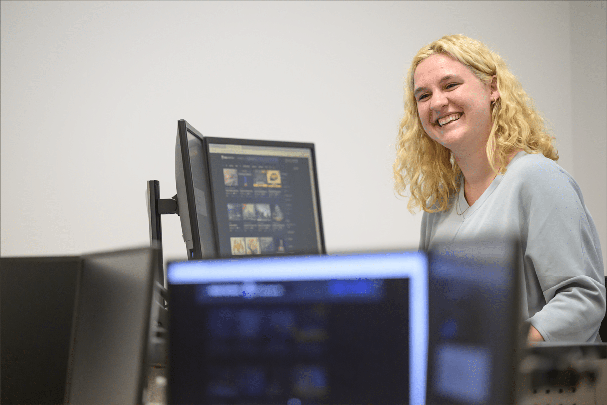 woman standing at a computer screen smiling.