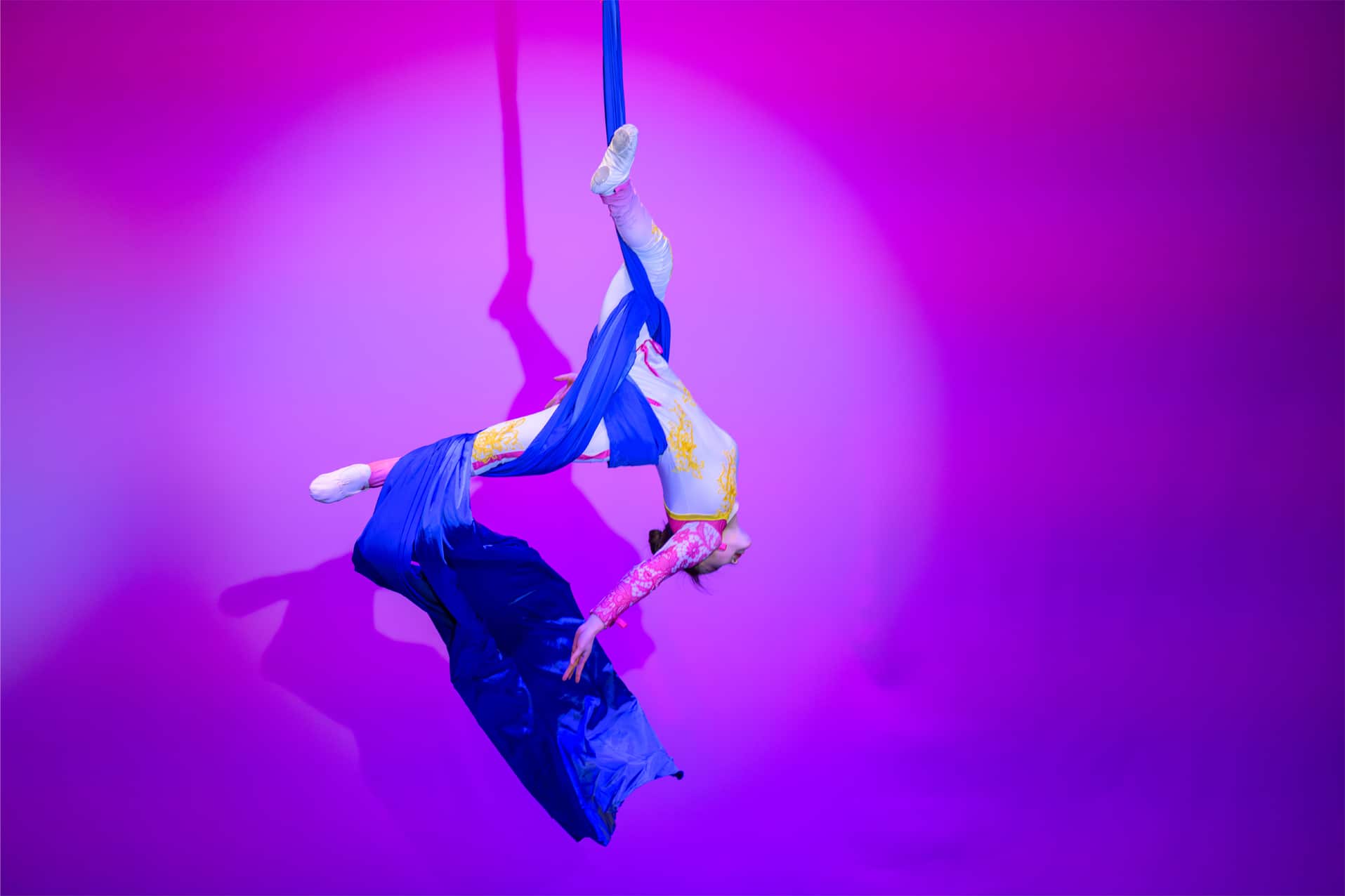 Acrobat hanging upside down on theater stage by a ribbon