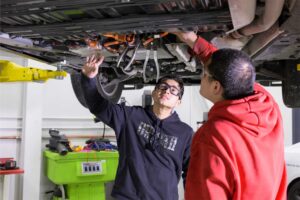 two students looking under a car