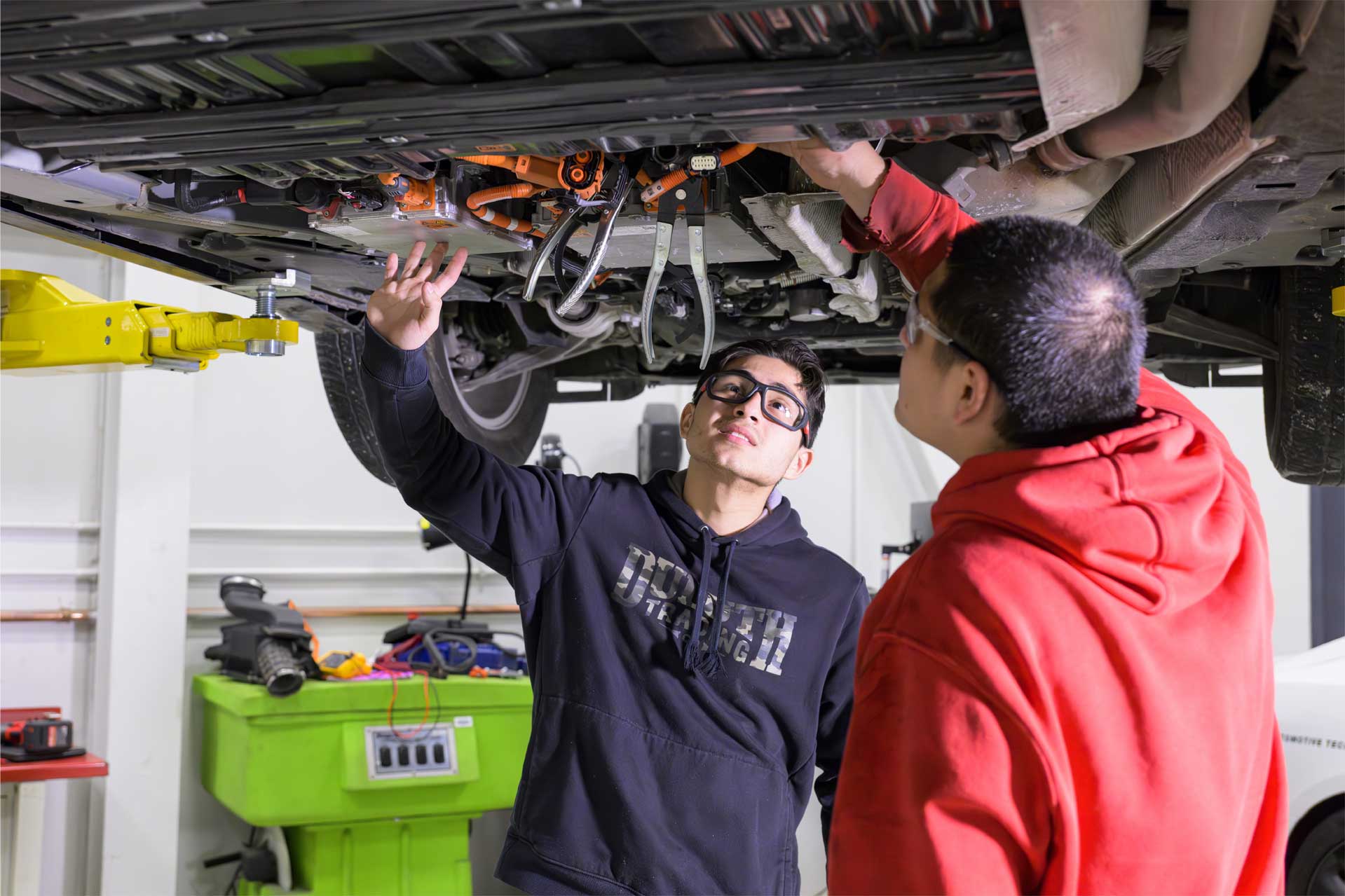 two students looking under a car