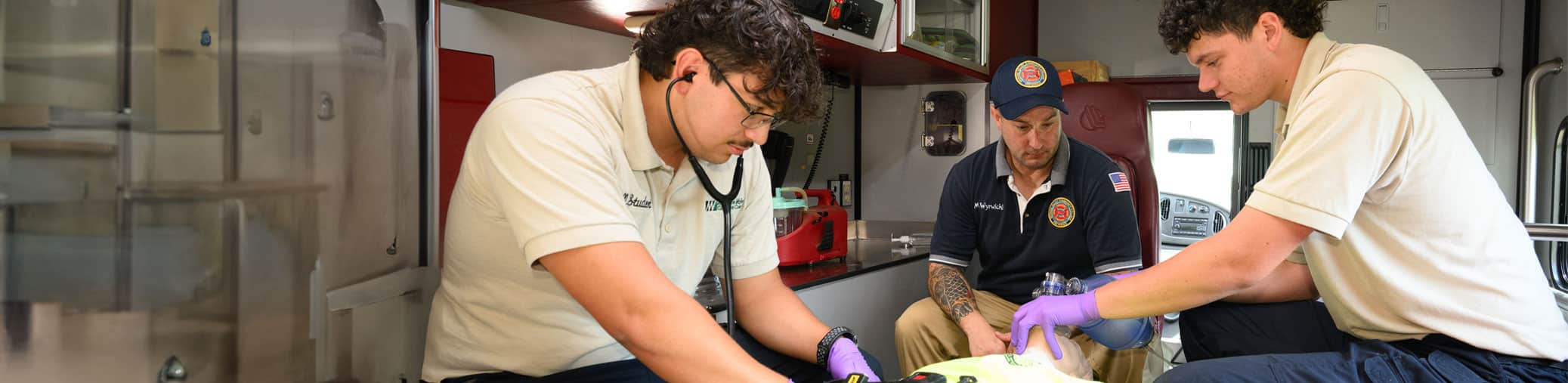 Two ems students working on a mannequin inside of an ambulance.