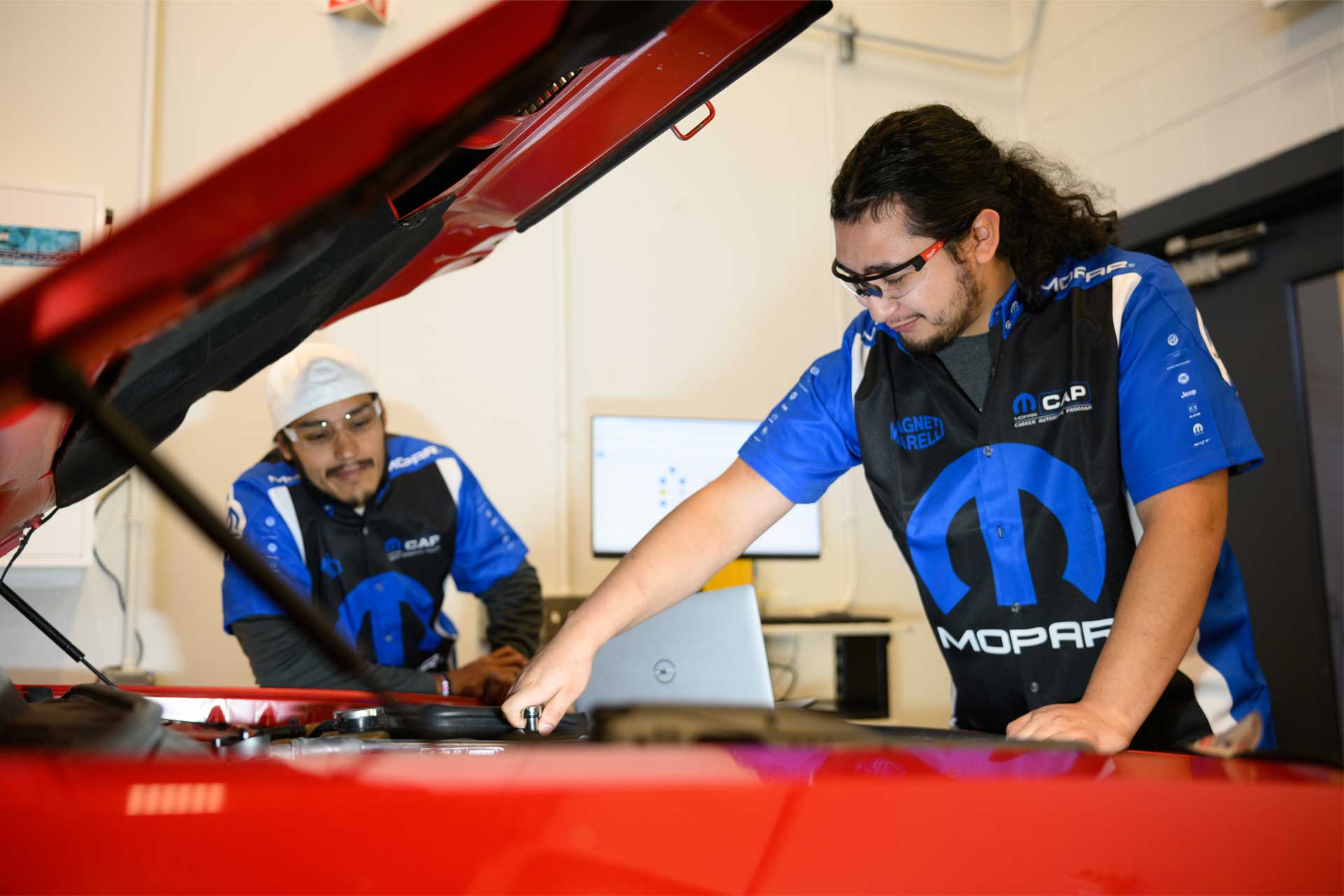 two students working under the hood of a car.