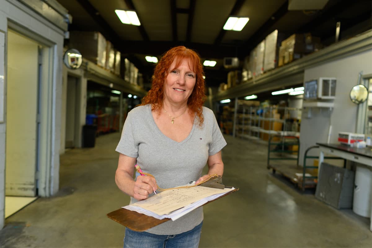 Red headed woman holding a clipboard in a warehouse.