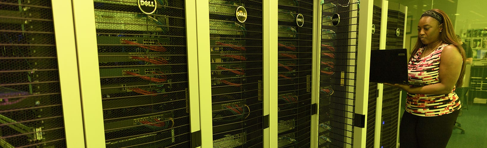 Person holding a laptop while standing in a server room with rows of equipment racks