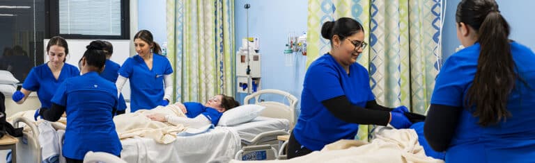 Students in blue scrubs working in a hospital simulation lab