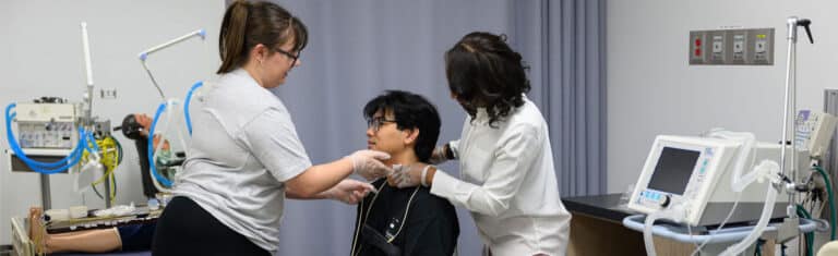 two students adding leads to a patient for a sleep technology test