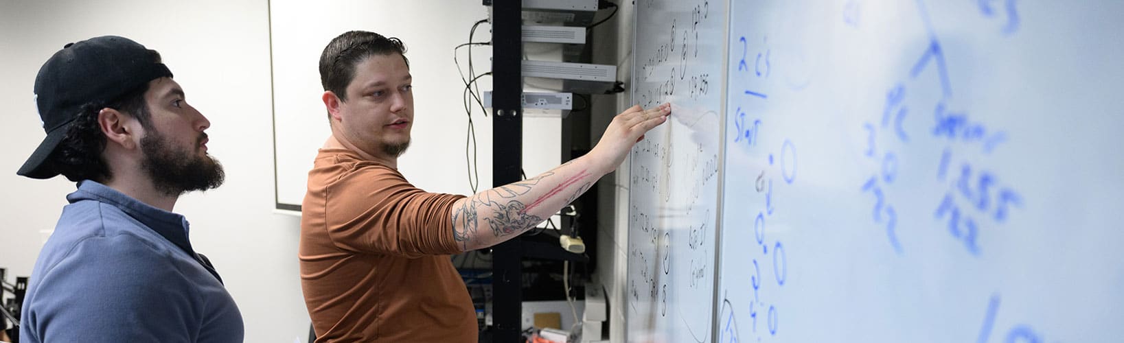 Two male students writing on a white board