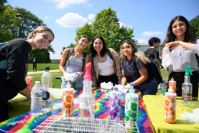 Students at a campus outdoor event doing tie-dye crafts at a table.