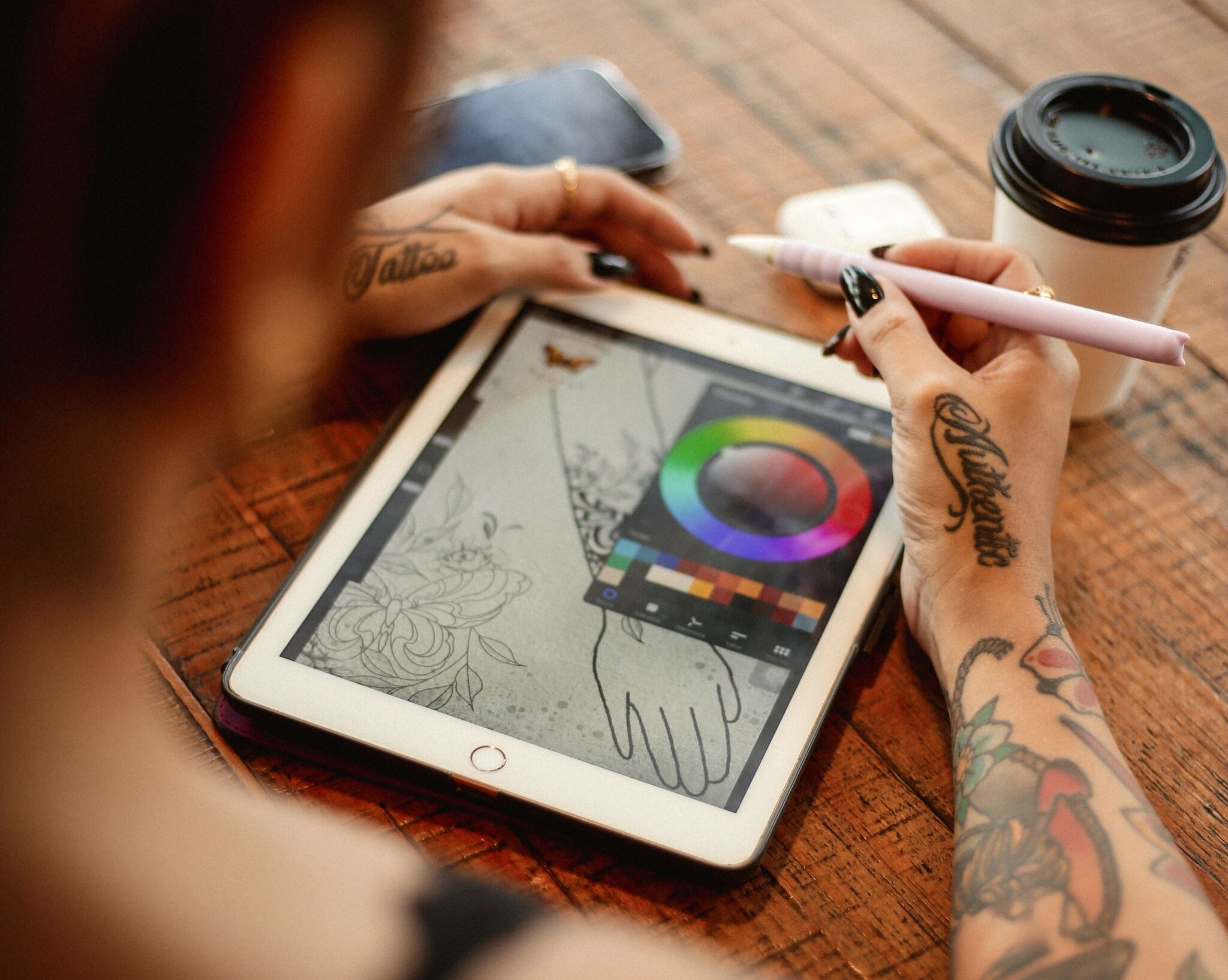 female artist using tablet and stylus for digital drawing. Coffee nearby.